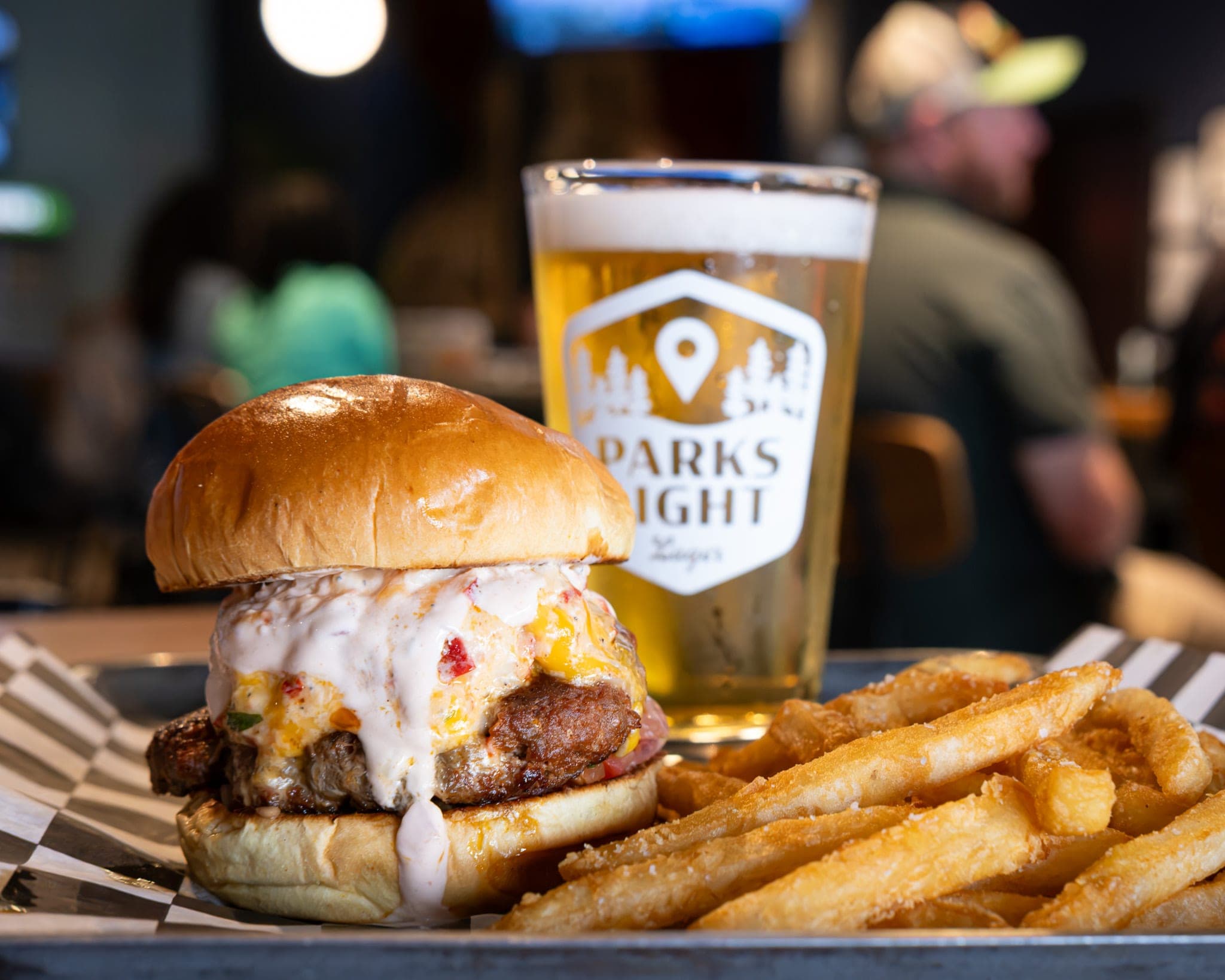 Burger topped with melted pimento cheese, with fries and a Parks Light pint